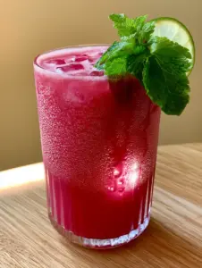 A close-up shot of an elegant ribbed glass with frosty condensation containing smooth magenta watermelon drink and clear ice cubes. (watermelon drink)
