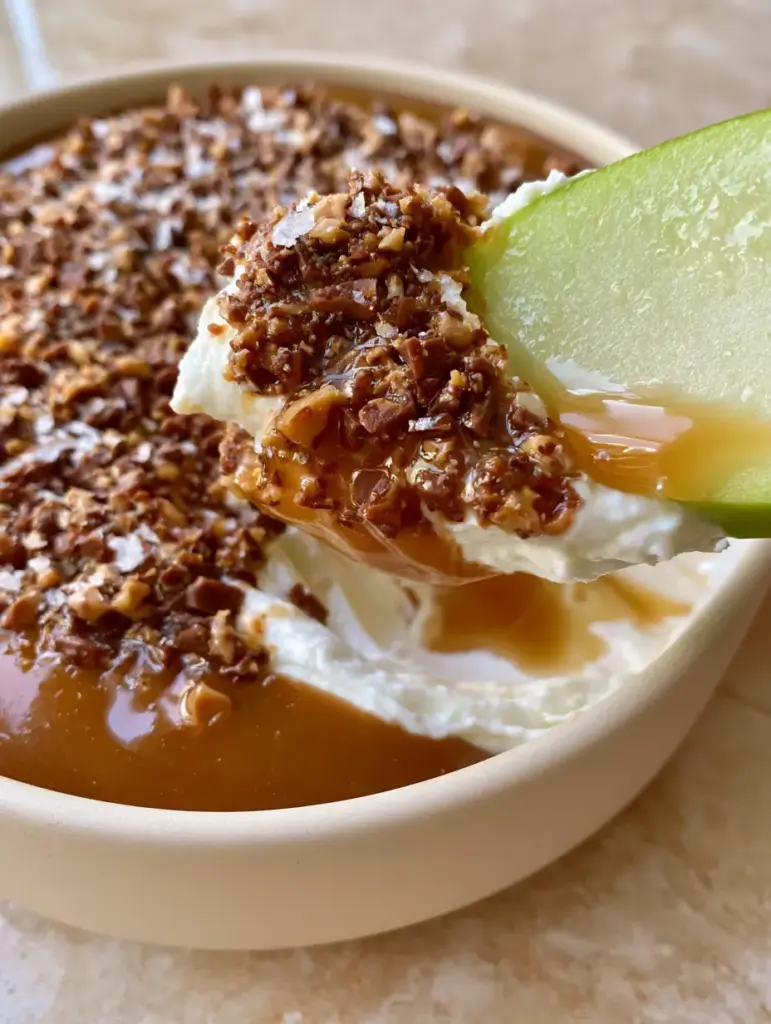 Overhead view of a minimalist bowl filled with apple toffee dip, showcasing the texture of English toffee bits and sea salt.