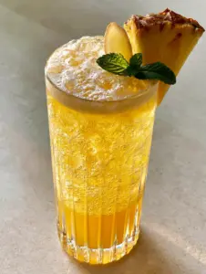 Close-up eye-level shot of a Pineapple ginger beer mocktail in a tall glass with glistening ice and froth. (Pineapple ginger beer mocktail)