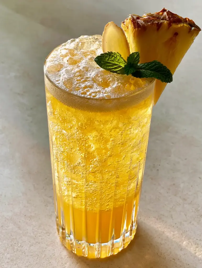 Pineapple Ginger Beer Mocktail: The Ultimate Sparkling Tropical Refresher 2 Close-up eye-level shot of a Pineapple ginger beer mocktail in a tall glass with glistening ice and froth. (Pineapple ginger beer mocktail)