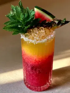 Macro photography of a Watermelon pineapple chill mocktail in a ribbed glass with visible condensation and a lime-zest sugar rim.