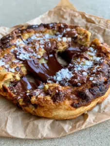 Close up handheld photo of a giant chocolate chip cookie being pulled apart with glossy dark chocolate stretching. (giant chocolate chip cookie)
