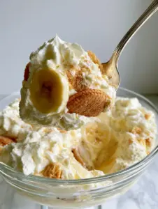 Macro photo of a silver spoon lifting a fluffy scoop of Magnolia Bakery banana pudding with stiff peaks of cream and crisp wafers.